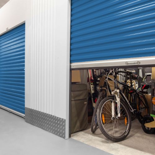 a metal roll up self storage unit door that is halfway open to reveal a unit filled with luggage, shelves, and household goods